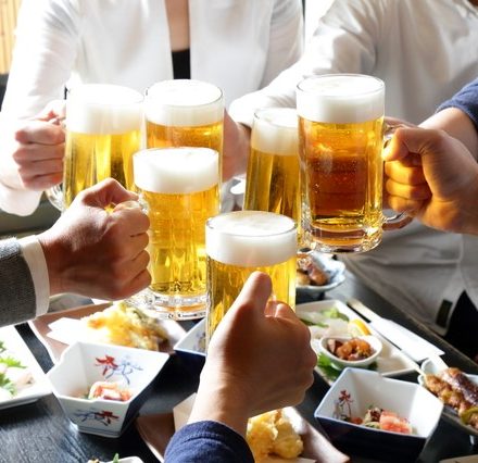 おつまみの乗ったテーブルの上でビールで乾杯する人々
