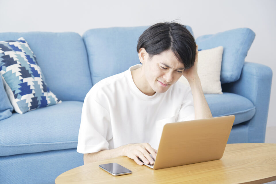 悩みながらパソコンで調べごとをする男性