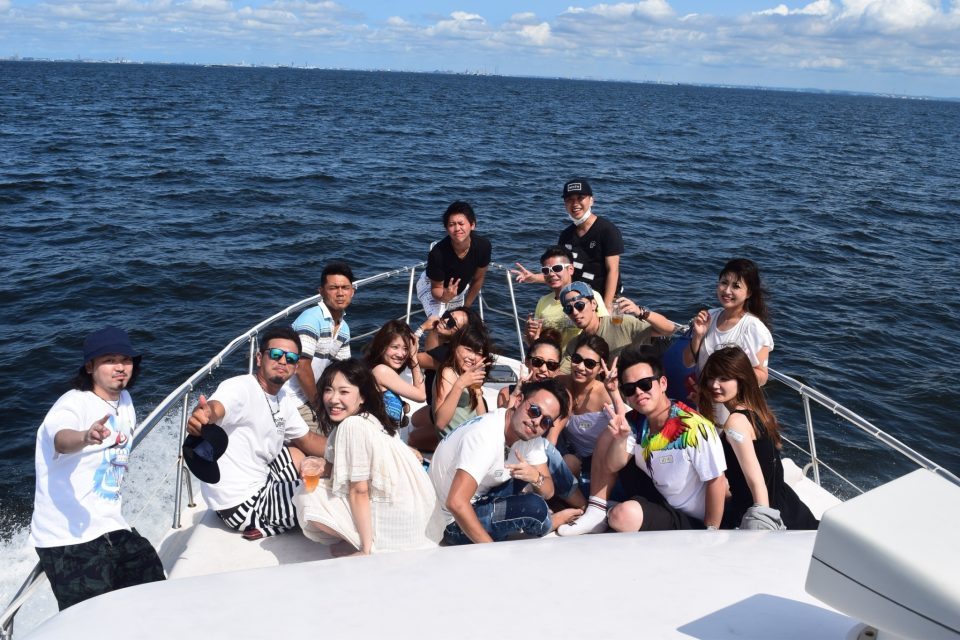 About 20 men and women taking a group photo with the ocean in the background on the front deck of *.