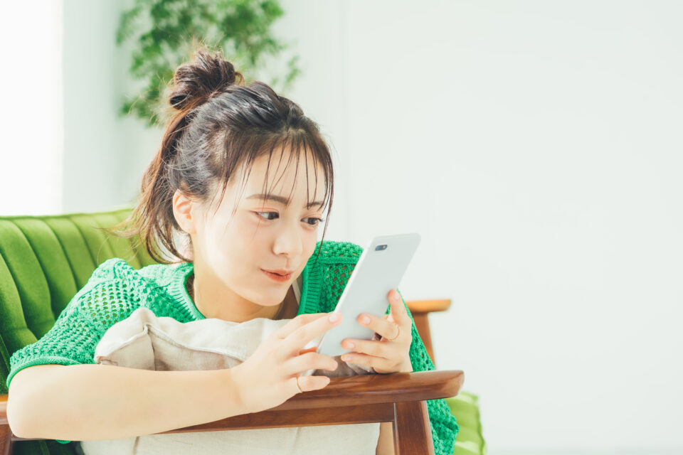 ソファに寝転がりスマートフォンを見る女性